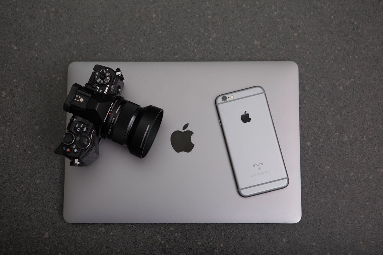 Home High-angle shot of DSLR camera, MacBook, and iPhone on textured surface, showcasing modern technology essentials.