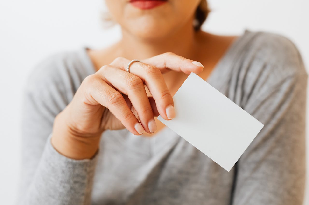A woman in gray sleeves holding a blank business card, perfect for presentation or mockup use.